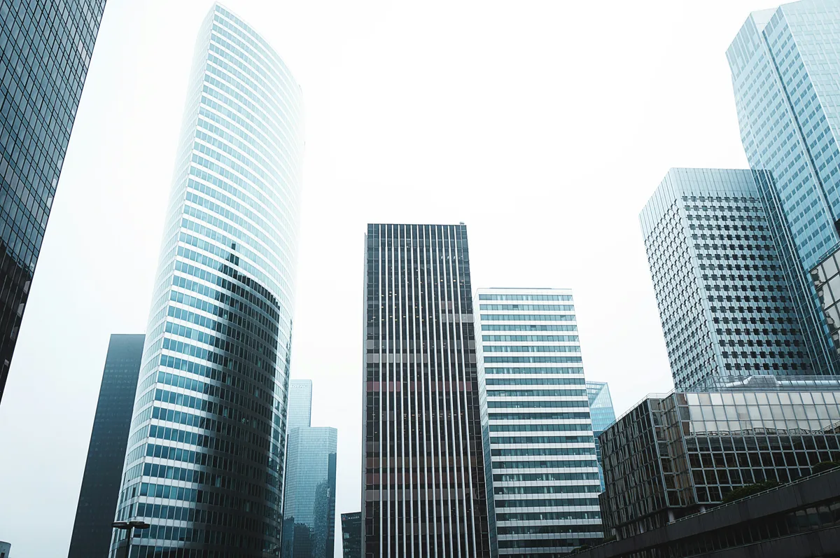 Glass office towers rising into an overcast sky, seen from street level