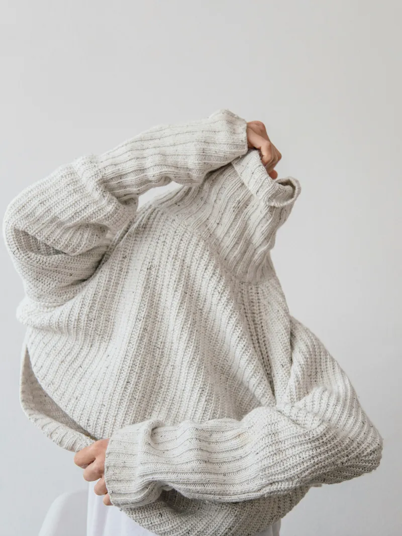 Person pulling on an oversized cream knitted sweater
