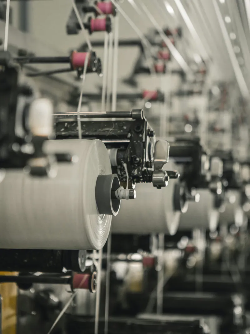 Spinning machine winding raw yarn onto bobbins in a textile mill, the material and fibre stage where fashion sustainability data begins